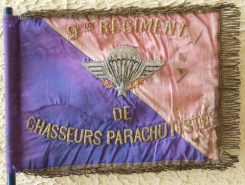A l' avers il est orné du Brevet de Parachutiste et de l'inscription  9° Régiment de Chasseurs Parachutistes en cannetille sur fond ROUGE ( parties flottantes )