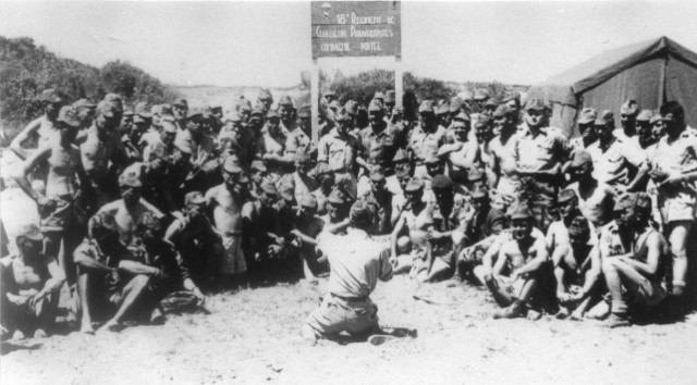 "Les parachutistes se regroupent autour des panneaux indiquant le bivouac des compagnies pour prendre des photos souvenirs .A gauche la Compagnie Portée autour du Capitaine WILLEMS. A droite la 4° section de la 2° Compagnie ."  