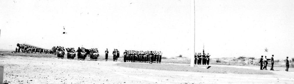 En arrière plan des parachutistes s' équipent sous les ailes d'un avion JUNKERS JU 52 .Au premier plan à gauche l'imposante musique du 18° R.I.P.C. au centre au "présentez armes "le Drapeau du 18° RIPC  et sa garde.A droite le Général Inspecteur  va passer en revue le détachement d'honneur qui n' apparait pas sur la photo."