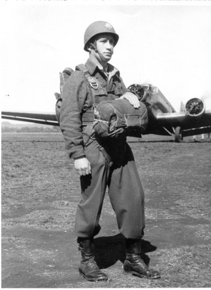 L'homme casqué est pret pour le saut ,il a bouclé autour de sa taille la sangle ceinture de fixation du dorsal .Son parachute T 5 est entièrement muni de sangles foncées .Sur son casque lourd U.S. le Brevet de l' Infanterie de l' Air  peint Blouson et pantalon modèle 45 Français