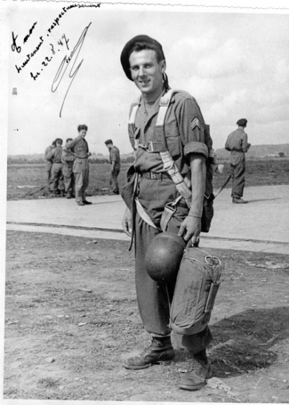 Le beret de ce Sergent Chef  à la mode des années 40 est porté incliné du mauvais coté  .Il porte une chemise en toile épaisse et un pantalon de drap Il est doté d'un casque lourd US et a aux pieds des chaussures US (?) derrière lui des camarades dans la même tenue sur une aire cimentée .