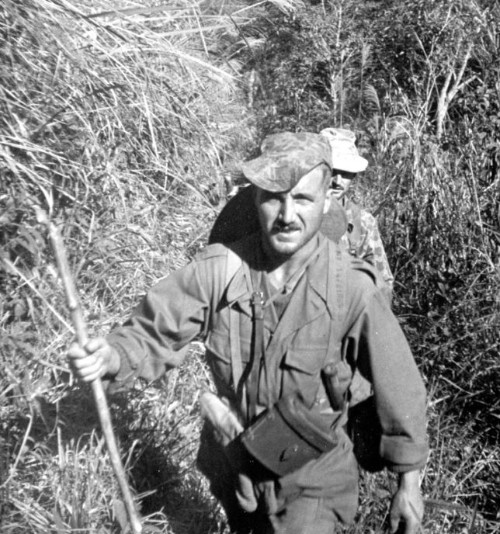 Canne en bambou en main droite un Officier Français coiffé de la casquette en usage au 8° Bataillon de Parachutistes Coloniaux et aussi semble t il au 1° LAO .L' étui porte jumelles en cuir est bien identifiable  . On reconnait la jugulaire de son chapeau de brousse ..il a donc simultanément deux coiffures .A son coté droit  un étrui PA en toile (britannique ) ,à son coté gauche le haut du manche d'une dague de type Commando"  