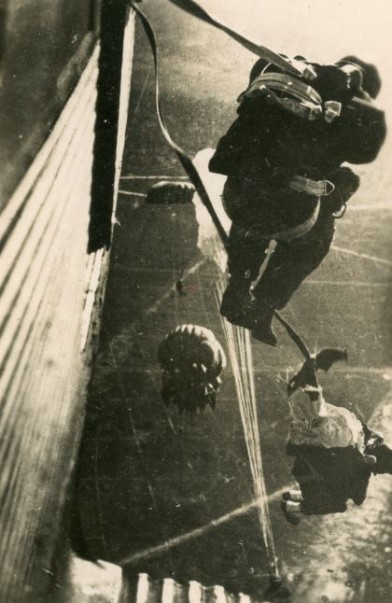 Deux sautants l'un en casque lourd , l'autre en casque personnel navigant en cuir. On voit l'ouverture, voile d'abord, du précédent parachutiste.